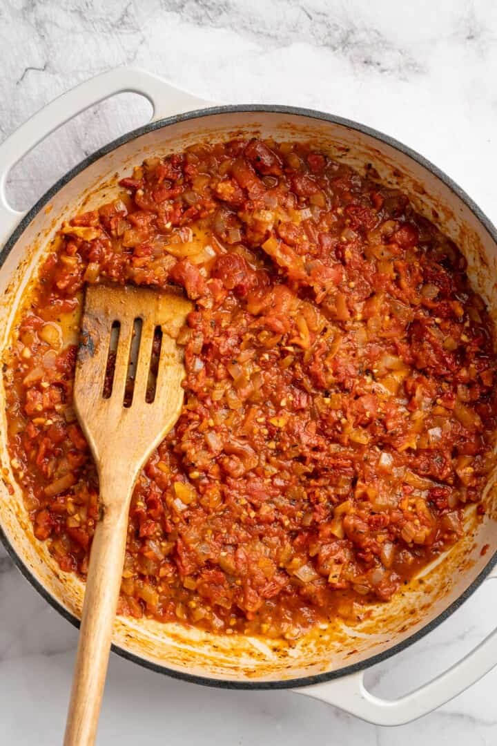 Overhead view of tomato sauce simmering in skillet with slotted spoon