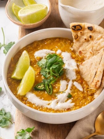 Bowl of homemade red lentil dal with naan, cilantro, and lime wedges