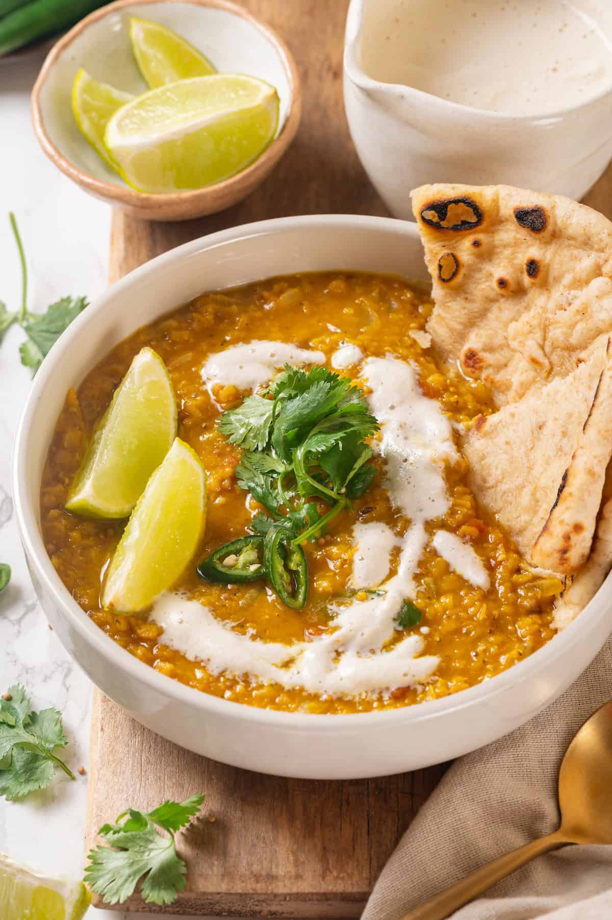 Bowl of homemade red lentil dal with naan, cilantro, and lime wedges