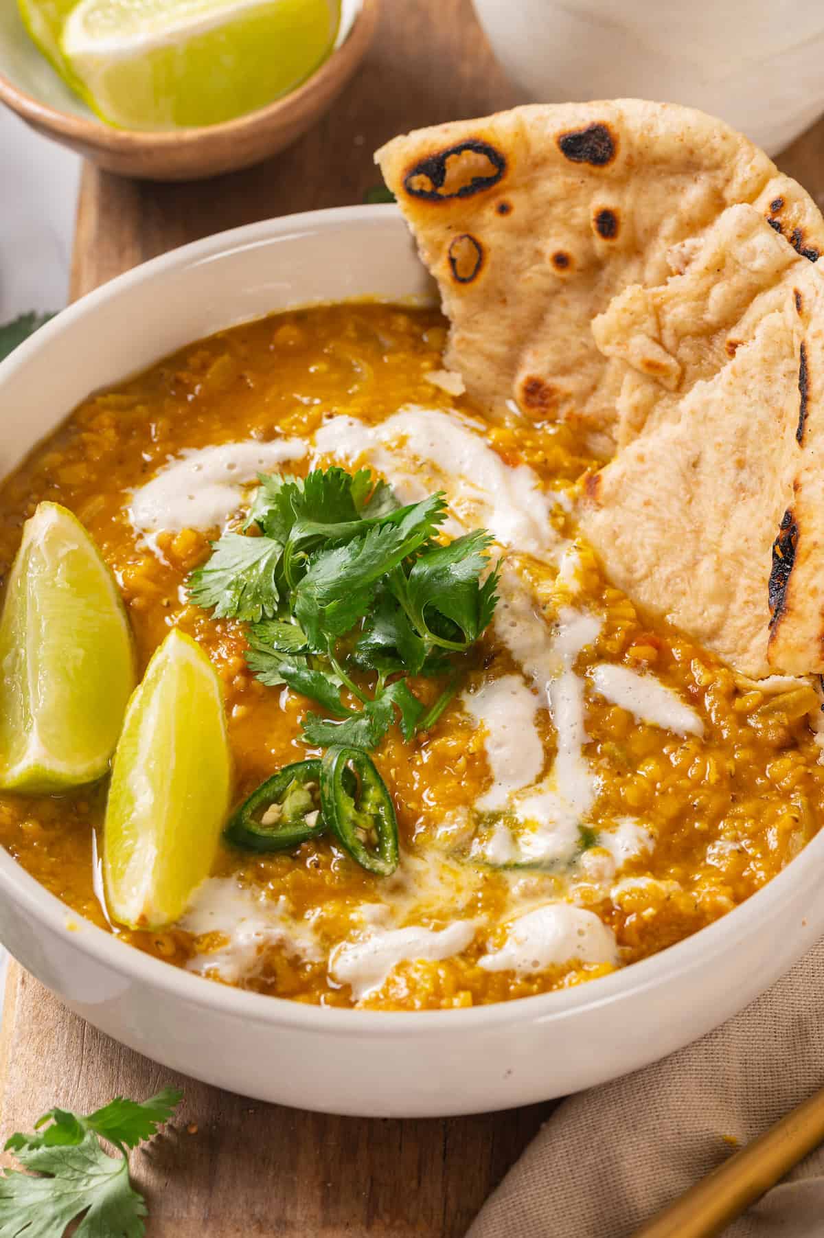 Bowl of red lentil dal with naan, lime wedges, and cilantro