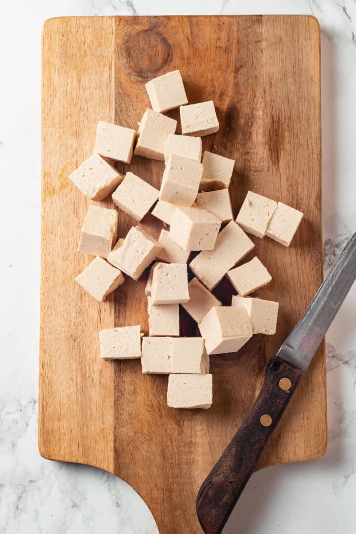 Cut tofu cubes on wooden board with knife