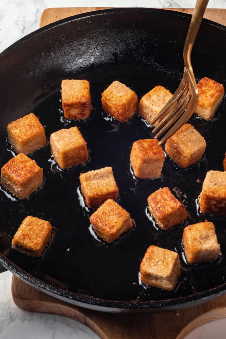 Fork about to pierce piece of tofu frying in skillet