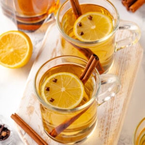 Two mugs of hot toddy with cinnamon sticks, lemon, and cloves