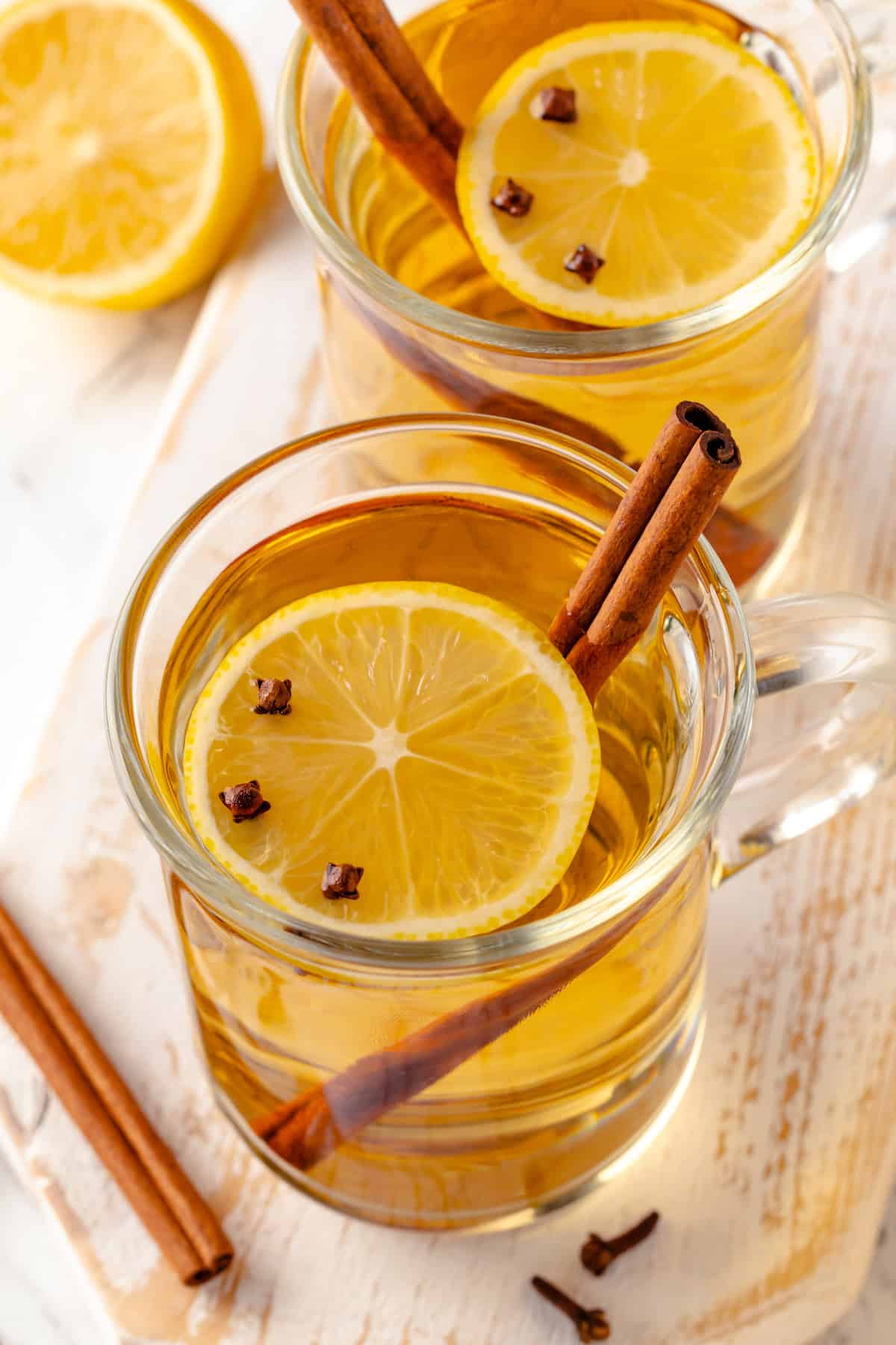 Two mugs of vegan hot toddy with lemon, cloves, and cinnamon stick