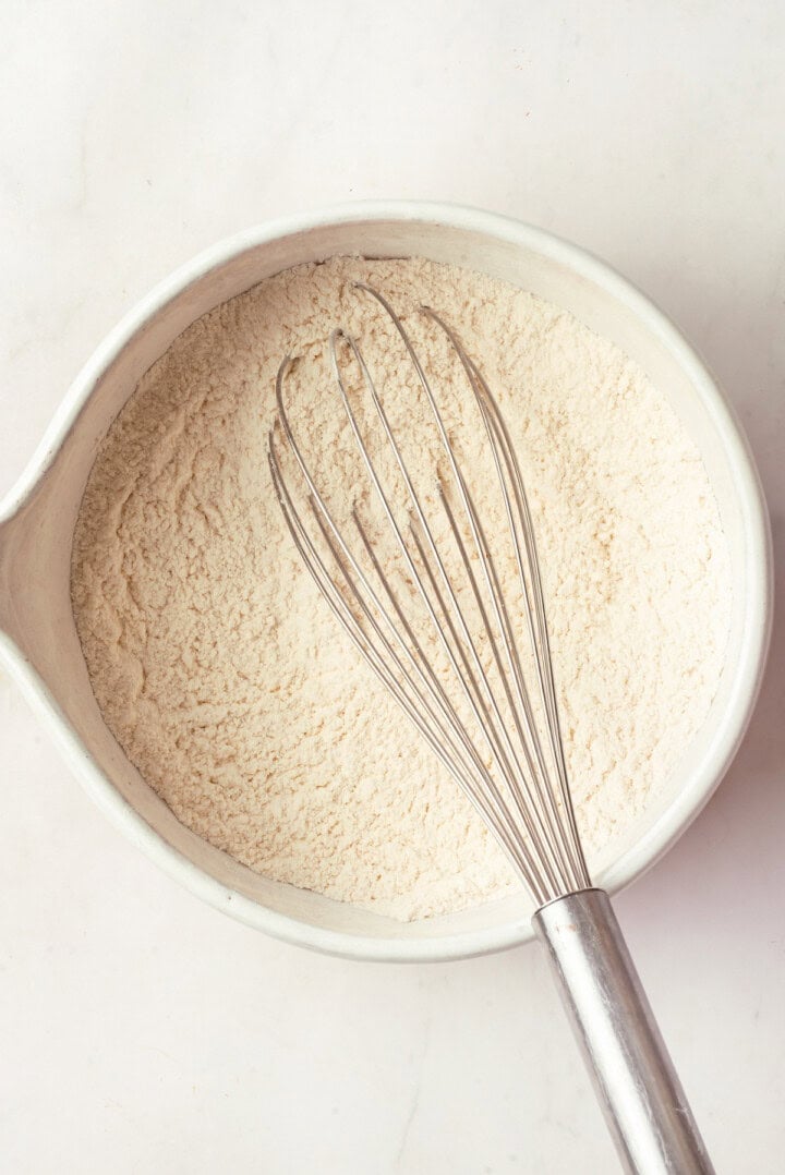 Dry ingredients for peanut butter cookies in mixing bowl with whisk