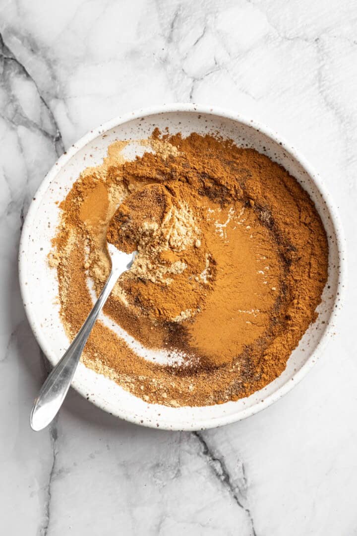Spoon stirring pumpkin pie spice in bowl