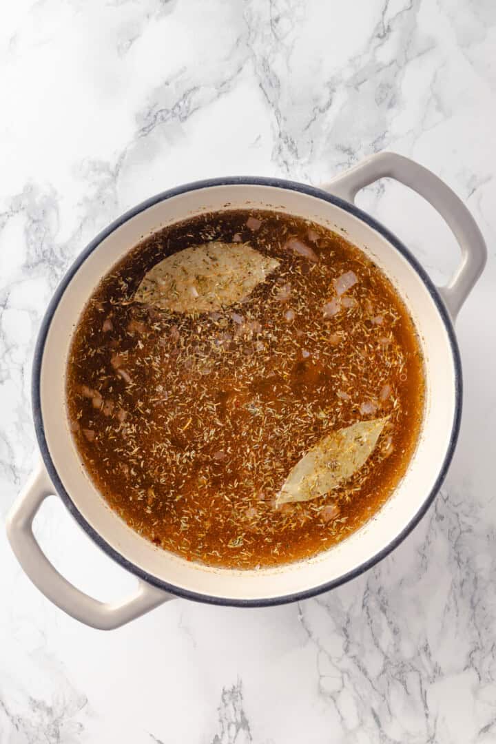 Seasonings and bay leaves added to soup pot with broth