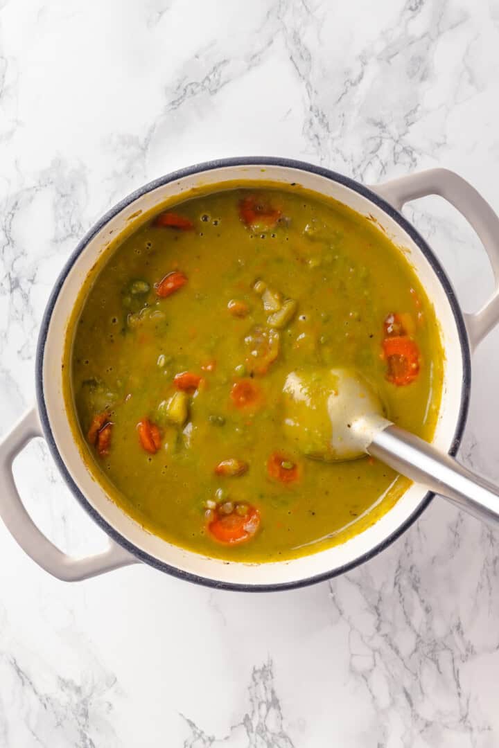 Overhead view of immersion blender in pot of pea soup