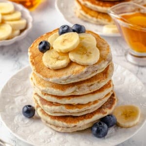 Stack of fluffy banana pancakes on plate with fresh fruit