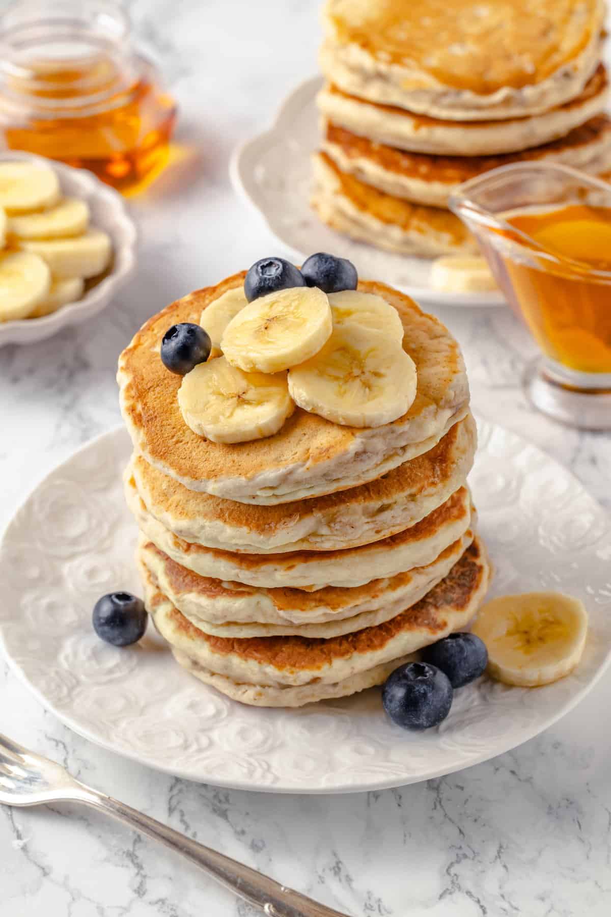 Stack of fluffy banana pancakes on plate with fresh fruit