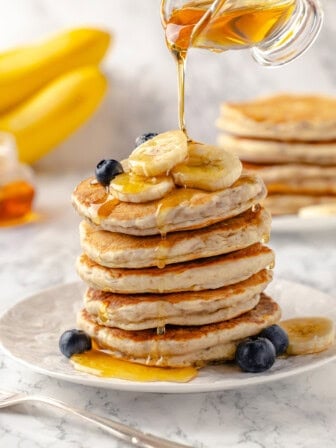 Pouring syrup onto stack of banana pancakes