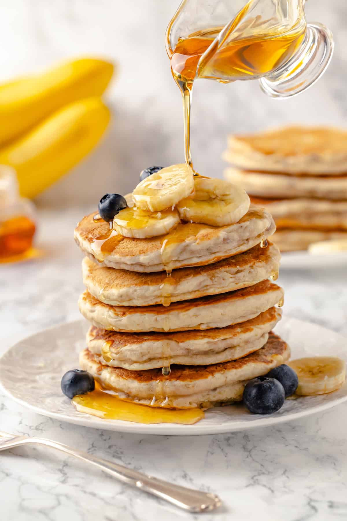 These fluffy banana pancakes are truly the best way to start your day! They're quick and easy, kid-friendly, and full of banana flavour. Pouring syrup onto stack of banana pancakes