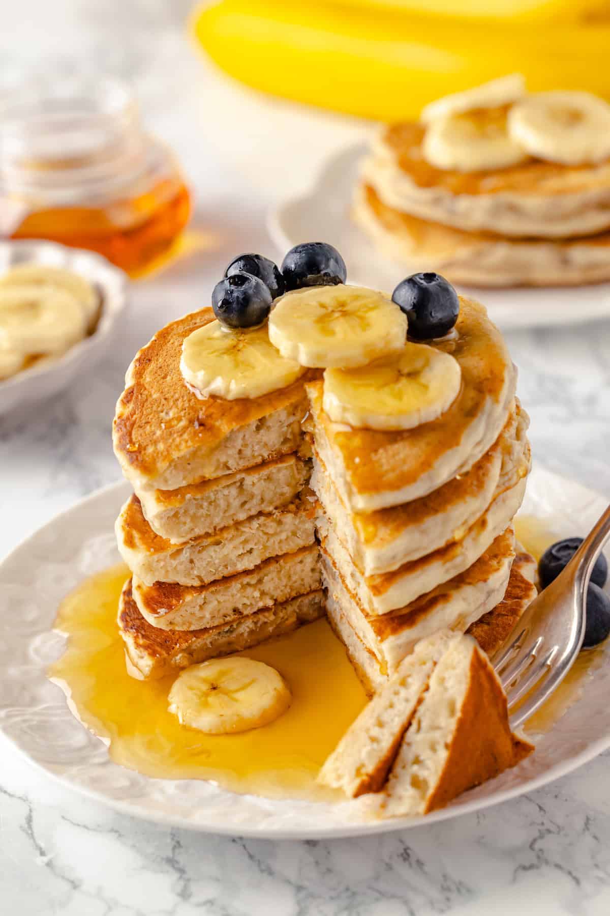 Stack of vegan banana pancakes on plate with syrup and fruit