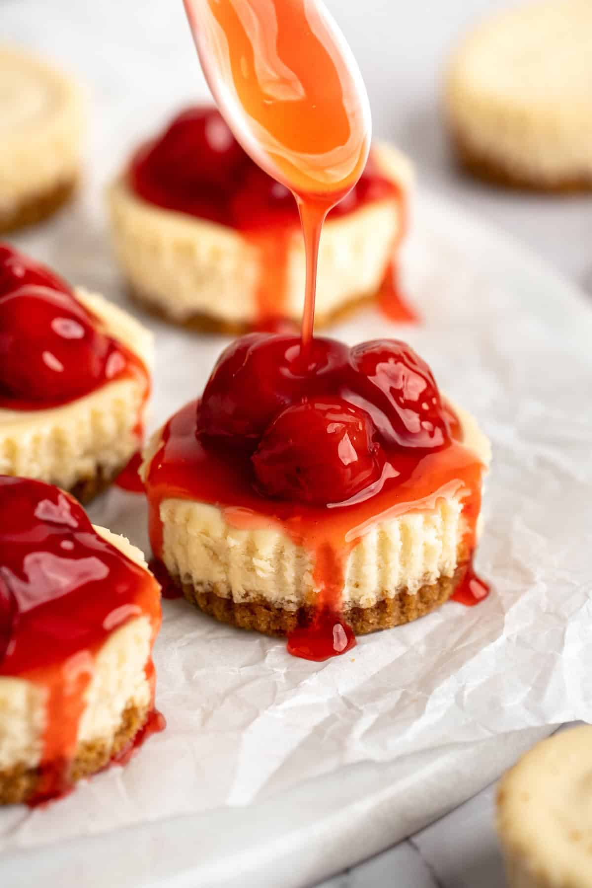 Drizzling cherry topping over mini cheesecakes