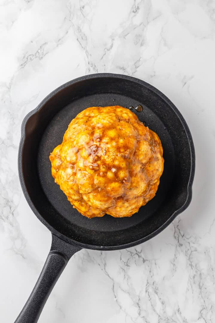 Butter mixture brushed onto cauliflower head in skillet