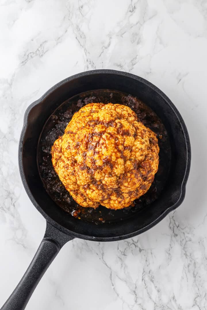 Overhead view of whole roasted cauliflower in skillet before adding cheese