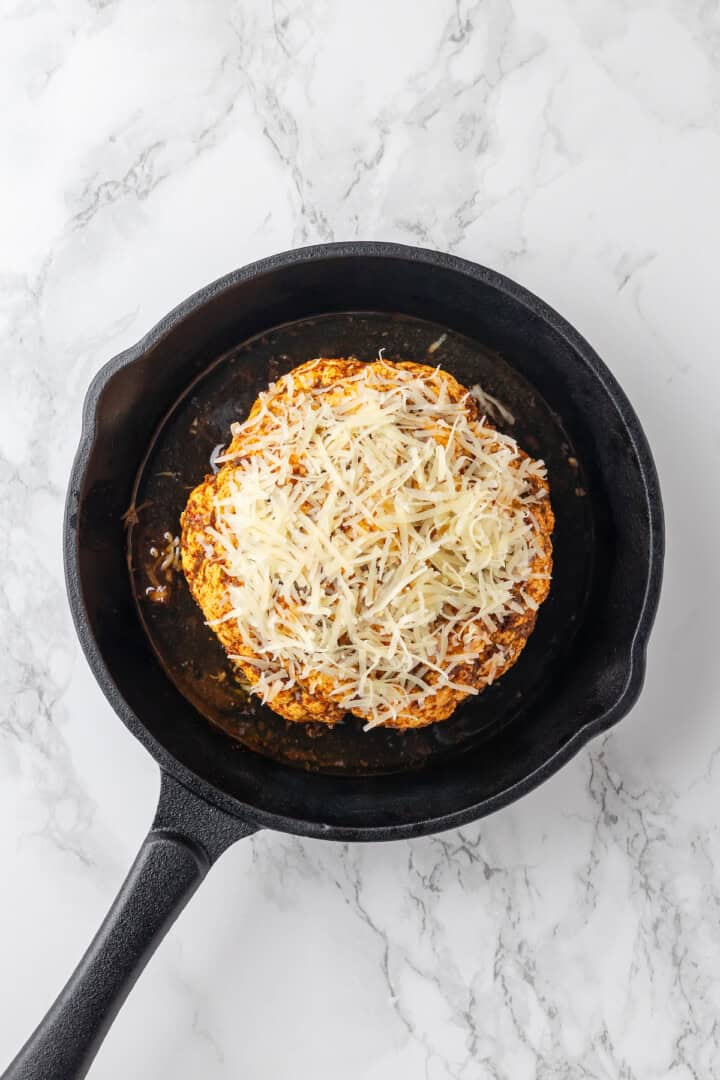 Overhead view of cauliflower head in skillet with vegan Parmesan sprinkled on top