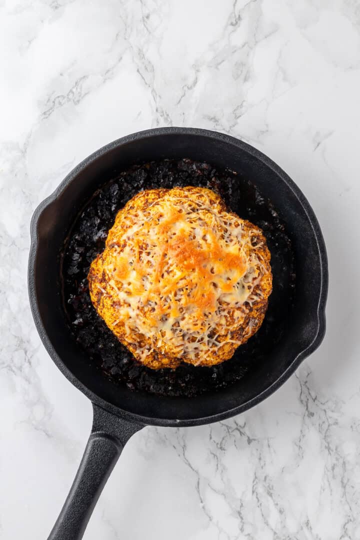 Overhead view of whole roasted cauliflower topped with vegan cheese