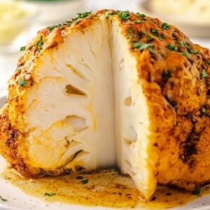 Whole roasted cauliflower on platter with wedge cut to show inside