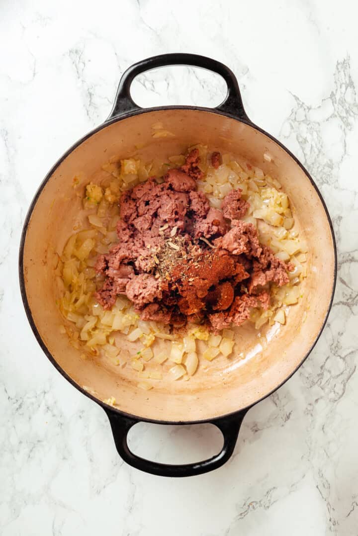 Seasonings and vegan sausage added to pot of sauteed onions