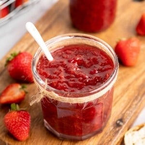 Two jars of homemade strawberry jam on wood board with fresh berries