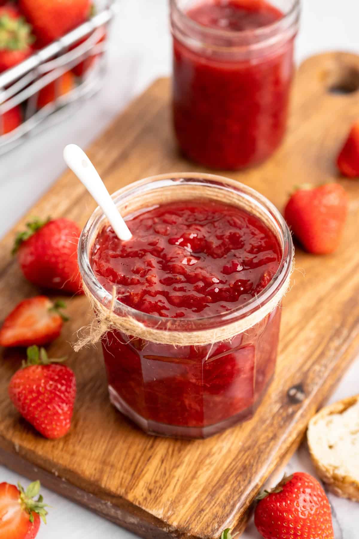 Two jars of homemade strawberry jam on wood board with fresh berries