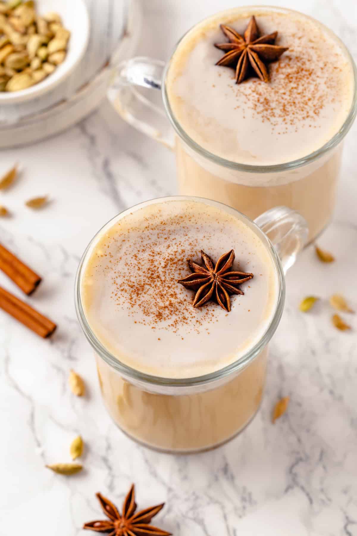 Top-down view of dirty chai lattes in 2 mugs with spices for garnish