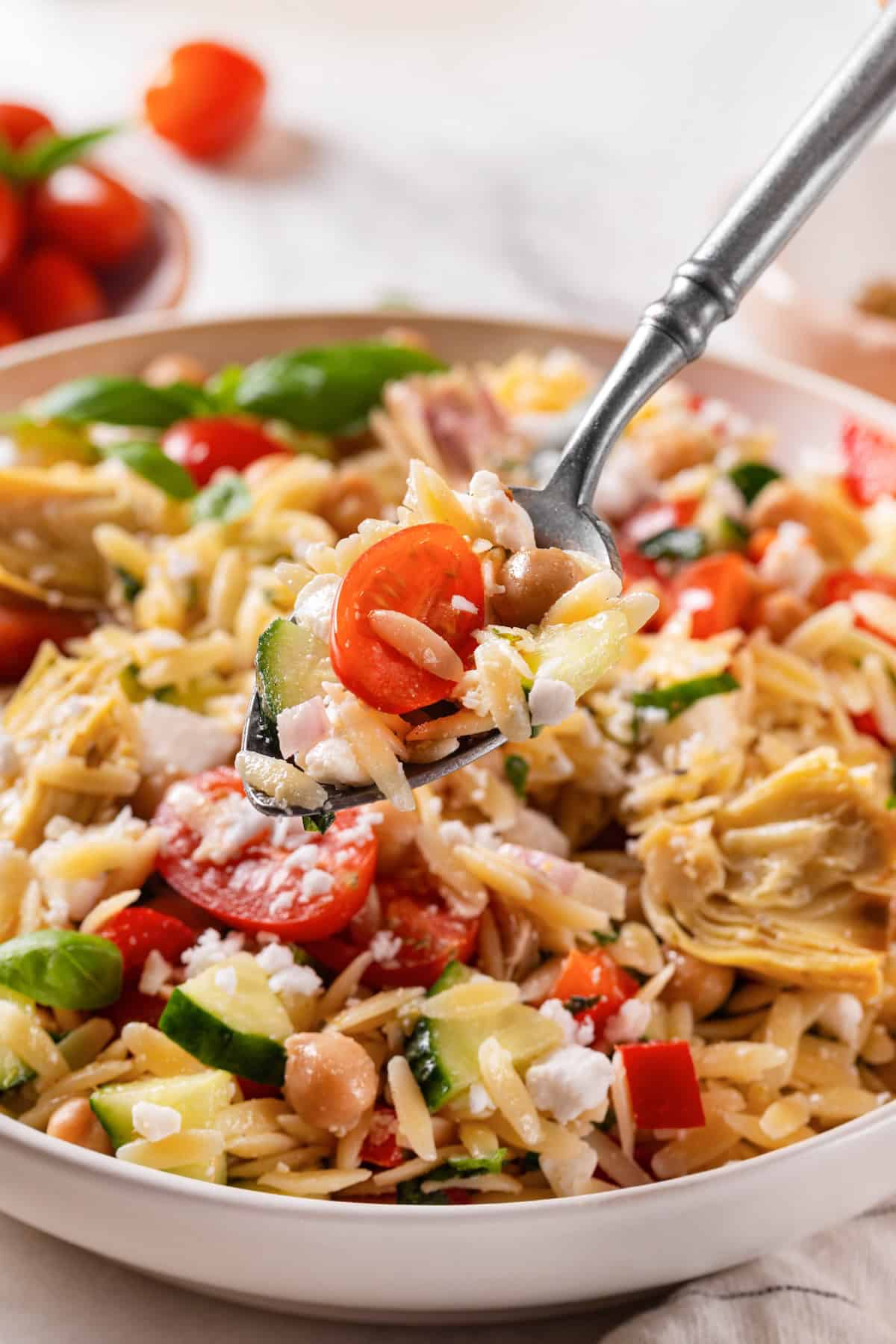Spoonful of orzo pasta salad held over bowl