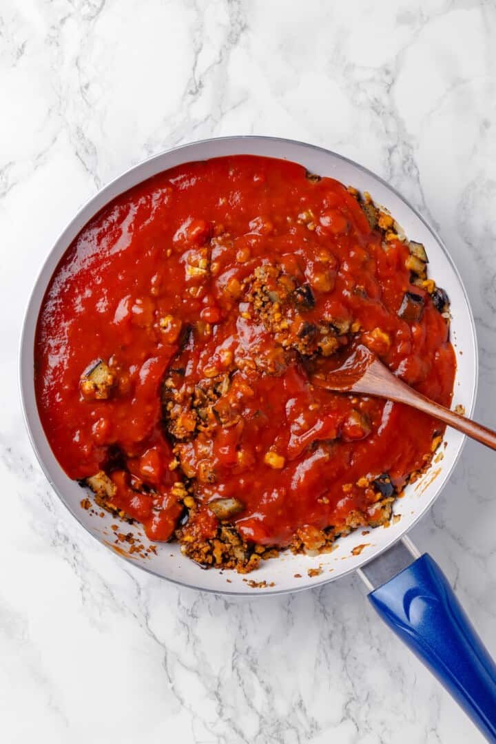 Stirring tomato sauce into vegan ground meat mixture