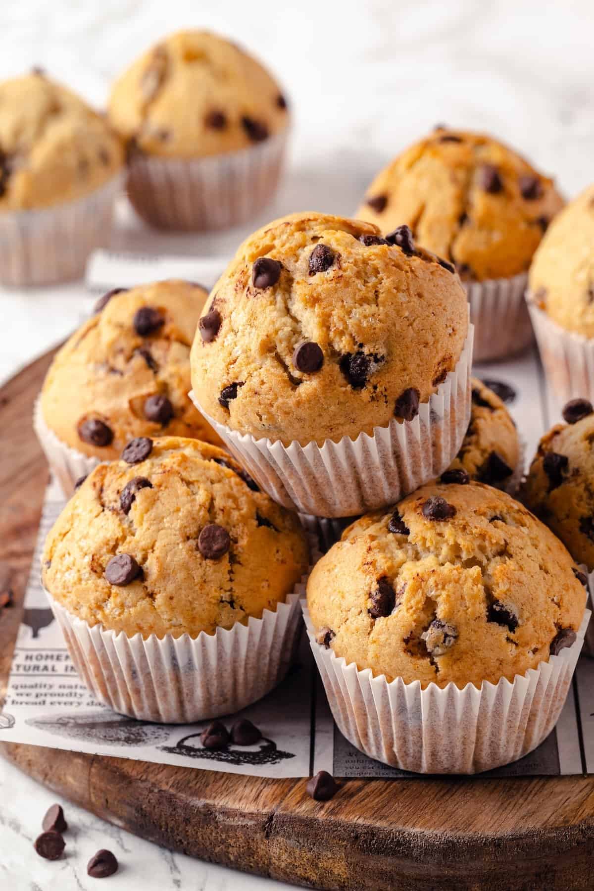 This moist and fluffy vegan chocolate chip muffin recipe is made with simple ingredients and easy enough that you can whip it up in minutes! Stack of chocolate chip muffins on wood board