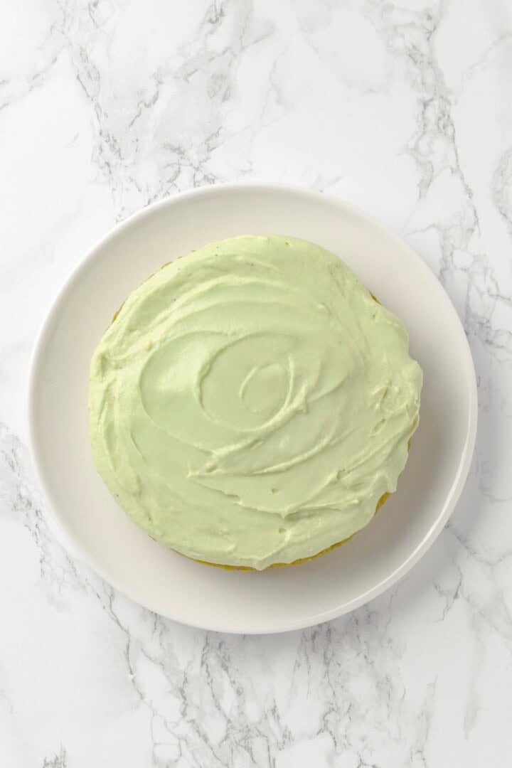 Overhead view of pistachio cake on cake plate before adding pistachio garnish