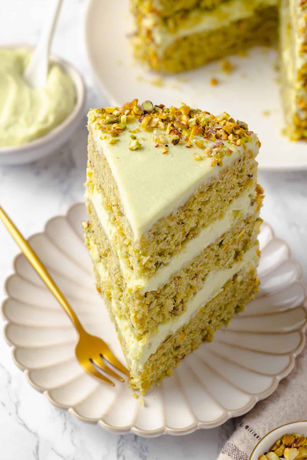 Slice of pistachio cake on plate with gold fork