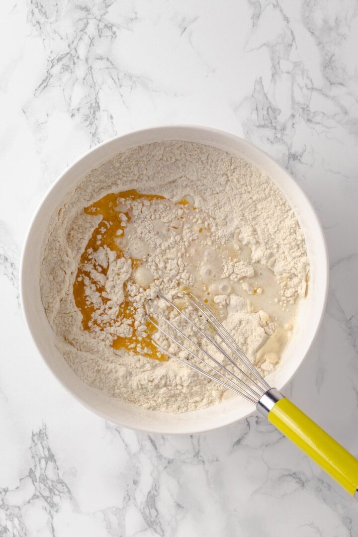 Overhead view of wet ingredients added to bowl of dry ingredients with whisk