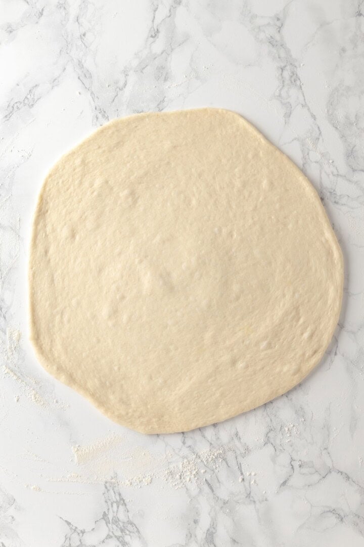 Overhead view of pizza dough rolled out onto marble countertop