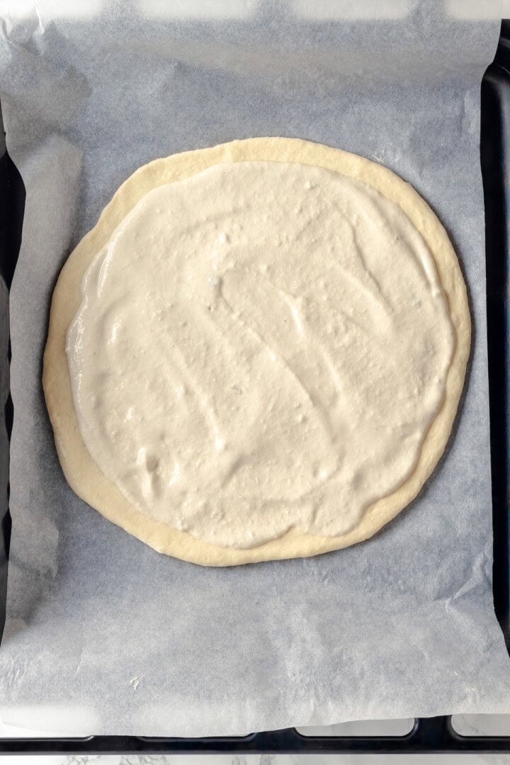 Overhead view of unbaked Alfredo sauce pizza on pan after adding sauce