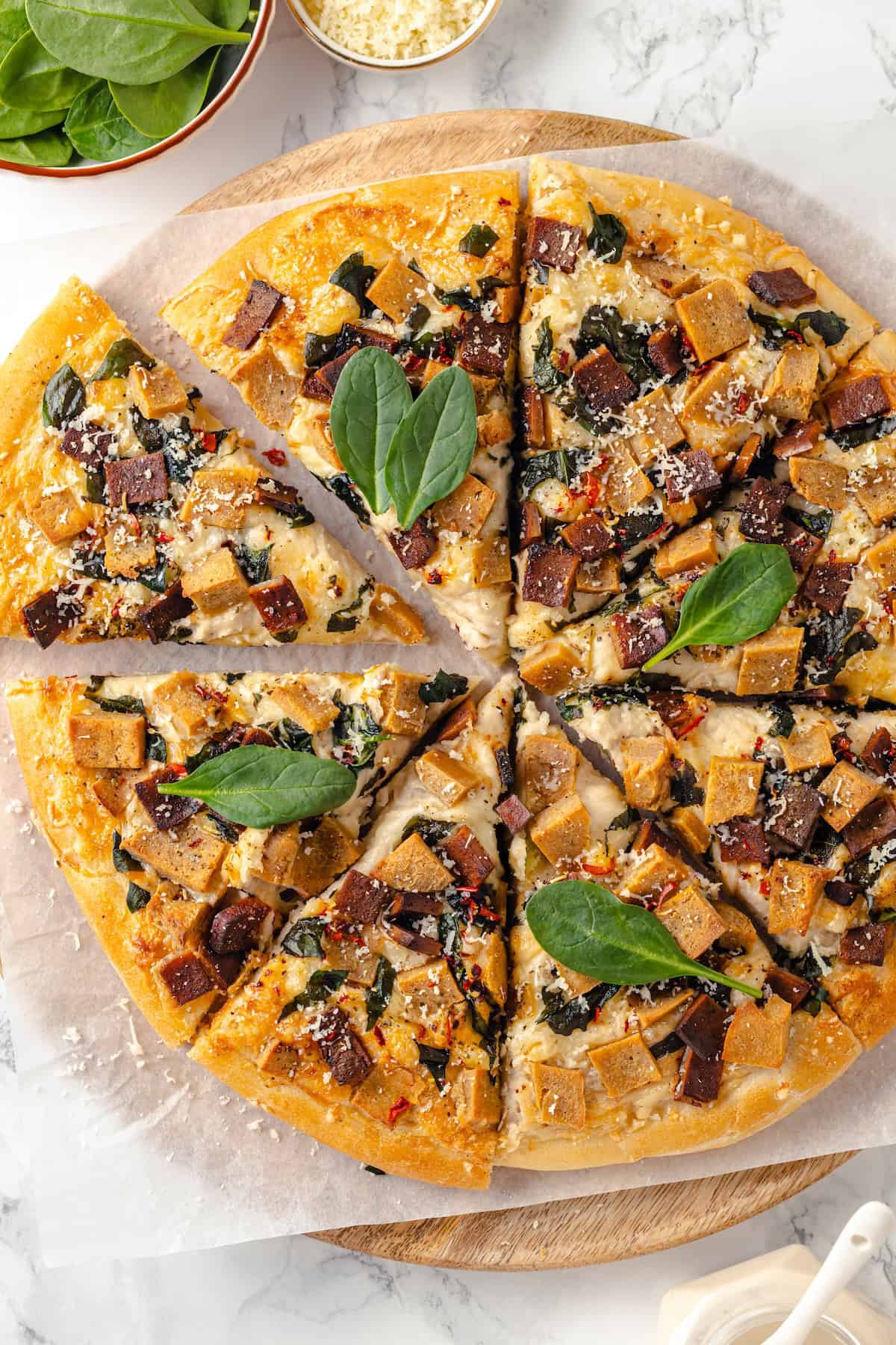A creamy sauce makes this Alfredo sauce pizza taste indulgent, but it’s vegan! Plant-based chicken and bacon take this recipe over the top. Overhead view of whole Alfredo sauce pizza cut into slices