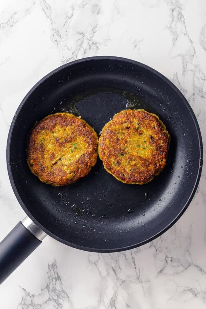 Overhead view of falafel burger patties cooking in skillet