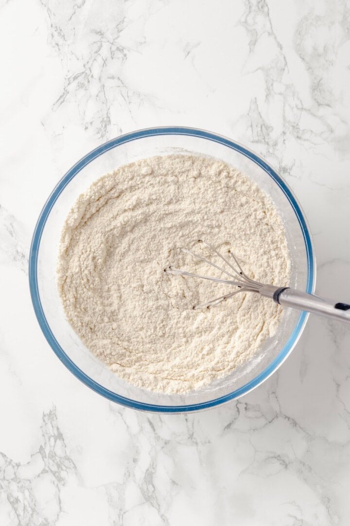 Overhead view of dry ingredients in glass bowl with whisk