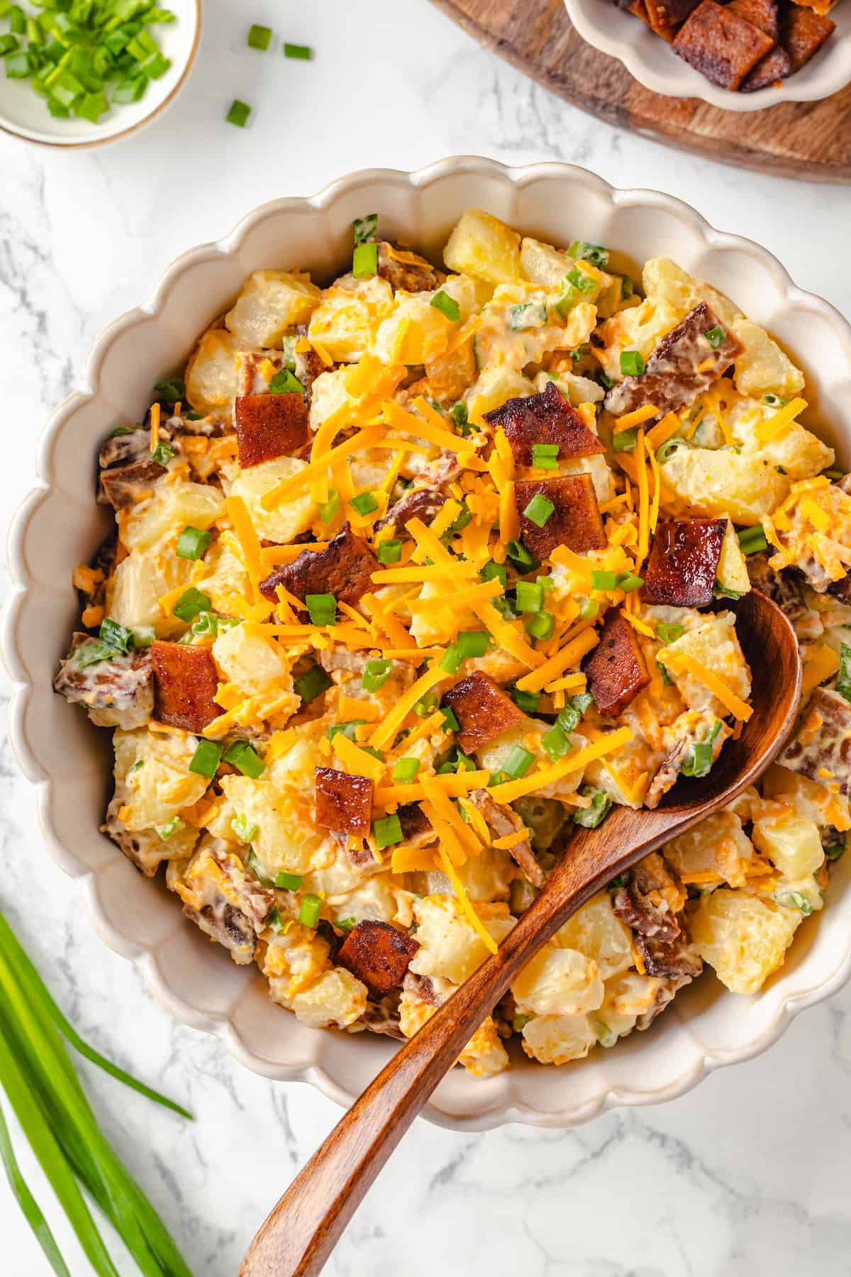 Overhead view of loaded baked potato salad in large bowl with spoon