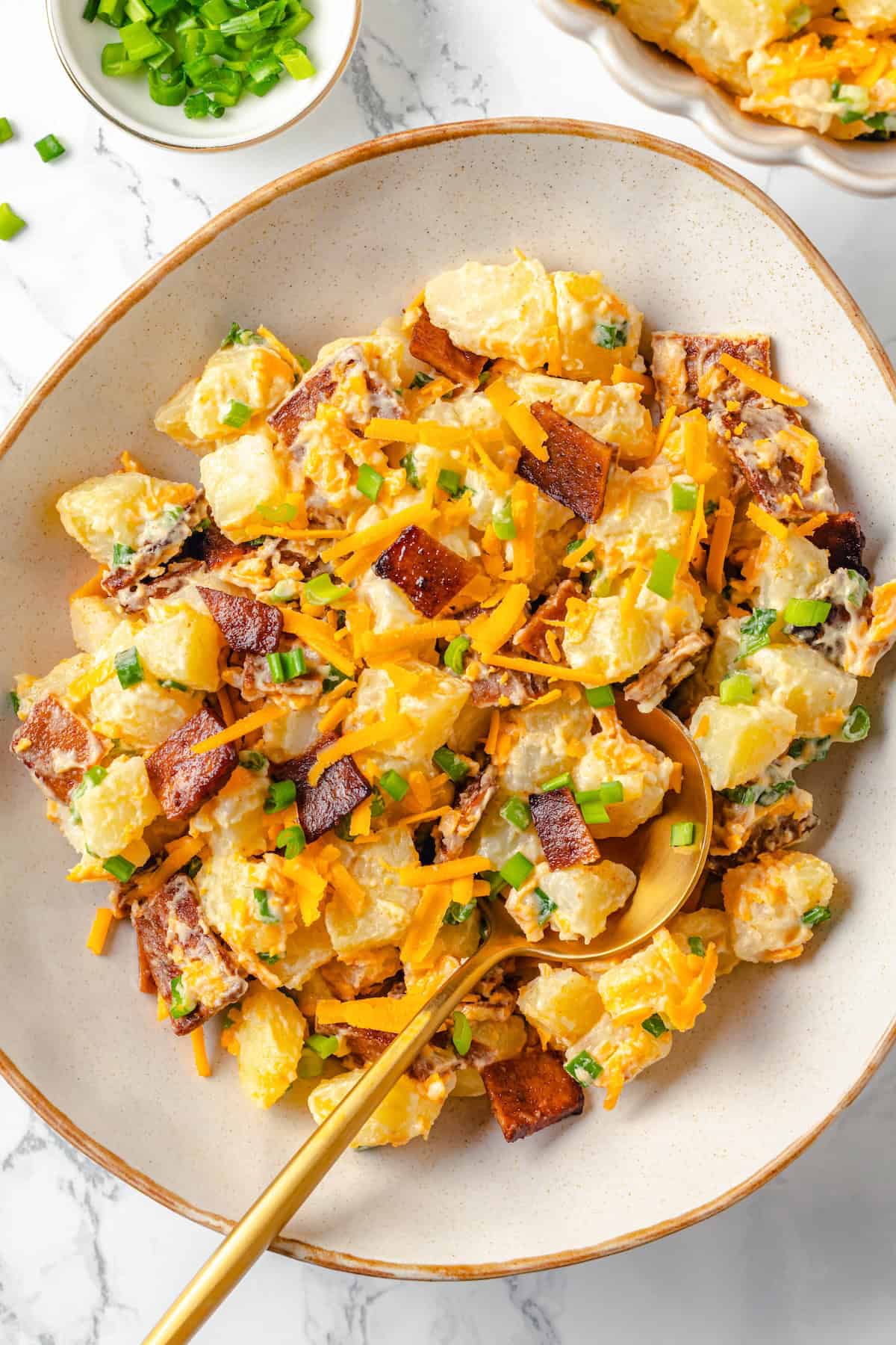 With potatoes, vegan bacon and cheese, and a creamy dressing, this loaded baked potato salad is the tastiest side for picnics and cookouts! Overhead view of vegan loaded baked potato salad in bowl with spoon