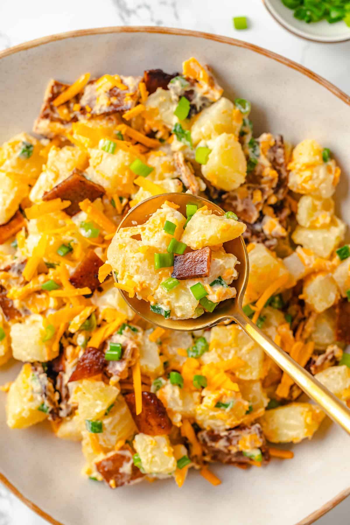 Spoonful of loaded baked potato salad held over bowl