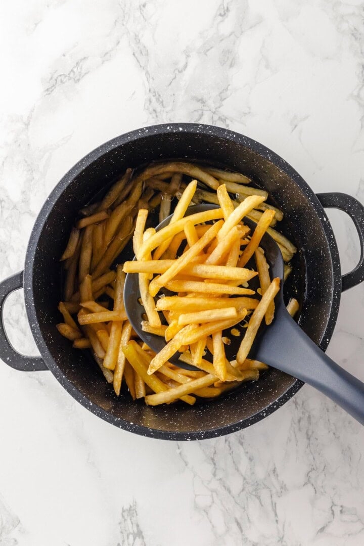 Overhead view of fries being removed from pot of oil