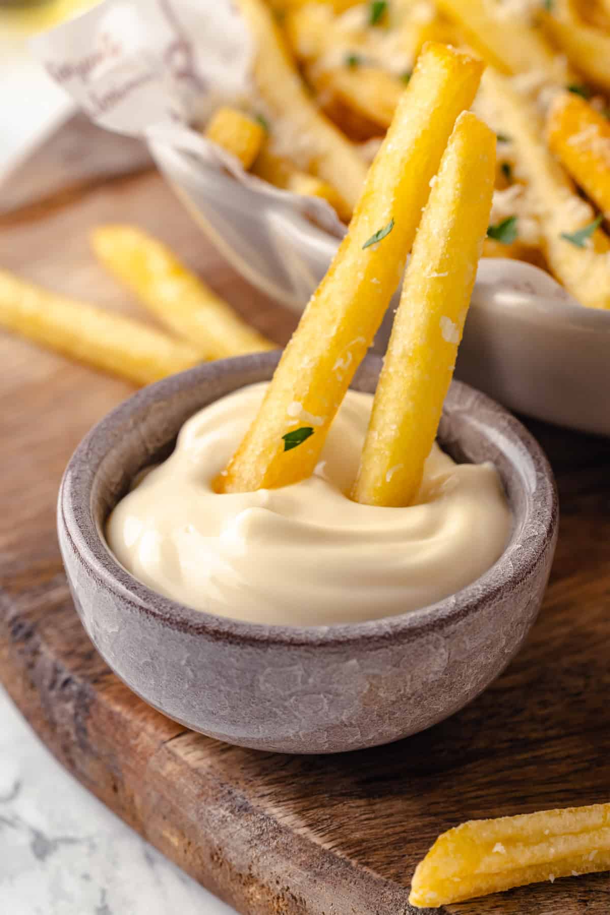 Two truffle fries dipping into bowl of aioli
