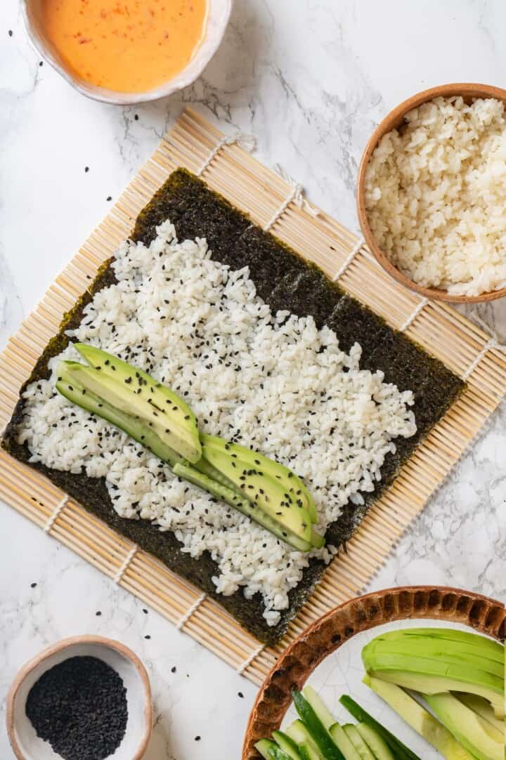 Overhead view of sushi rice, cucumber, and avocado on sheet of nori