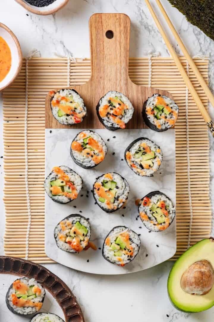 Overhead view of vegan avocado sushi on marble and wood serving board