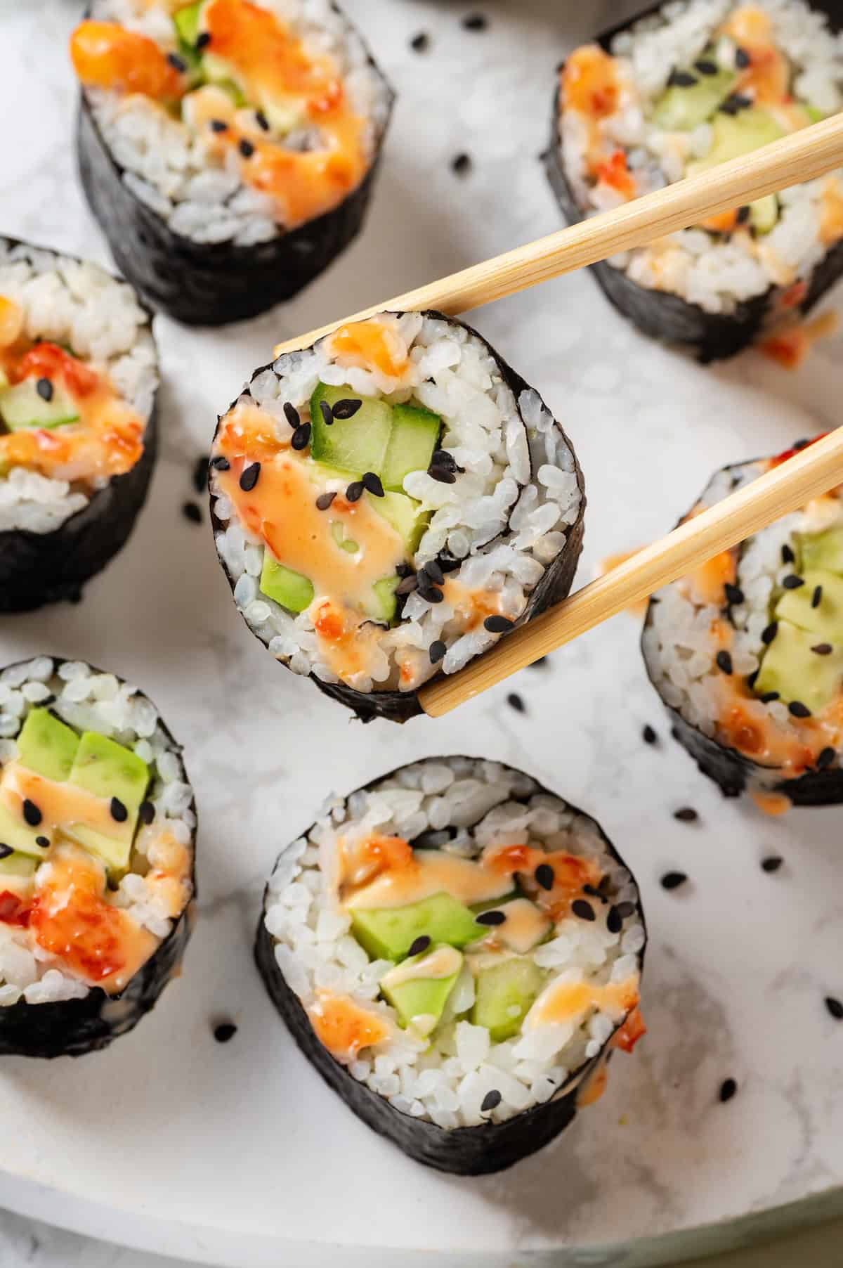 Chopsticks holding avocado sushi roll with bang bang sauce