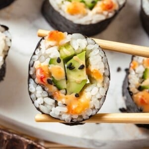 Chopsticks holding avocado sushi roll with bang bang sauce