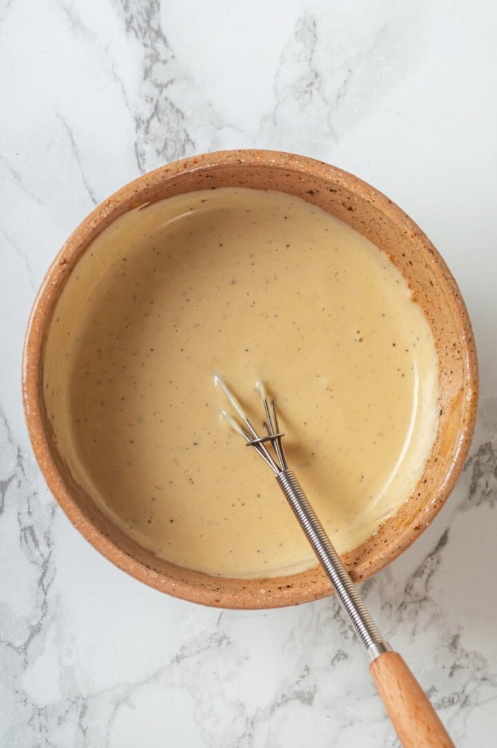 Overhead view of broccoli slaw dressing in bowl with whisk