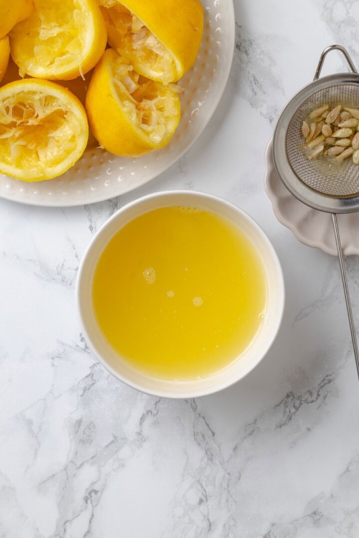 Overhead view of lemon juice in bowl next to plate of juiced lemons
