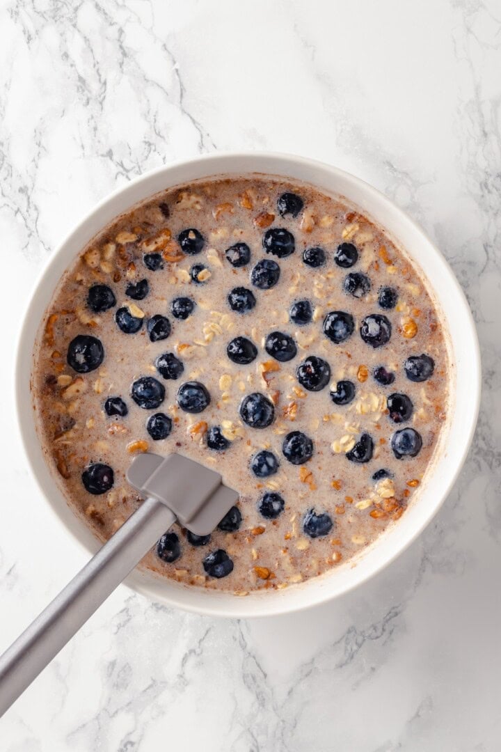 Overhead view of oatmeal and blueberry mixture in bowl with rubber spatula